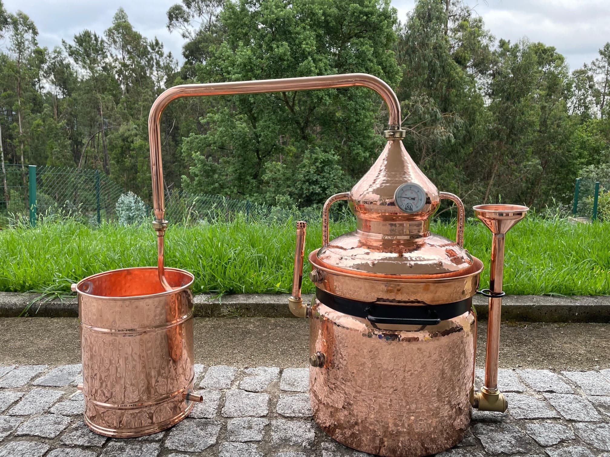 Double copper boiler, Copper helmet with swan neck, Condensing recipient with serpentine coil, quick release brass couplings between the helmet and swan neck and also between the swan neck and condensing recipient, the external chamber includes an entrance with a funnel for filling up with water and a brass plug near the base for discharging water. A spring thermometer is also included with all bain marie alembics.
